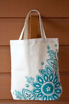 a white bag with blue flowers on it hanging from a wooden hanger against a brown wall