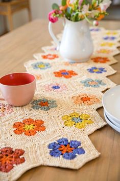 crocheted placemats on a wooden table with plates and flowers in the vase