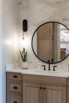 a bathroom sink with a large round mirror over it's counter top next to a potted cacti