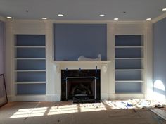 a living room with blue walls and white bookcases on the wall, in front of a fire place