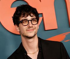 a man with glasses standing in front of an orange and blue sign that says gq