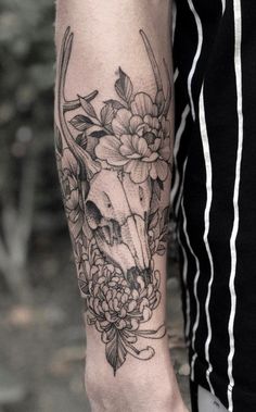 a person with a tattoo on their arm holding a deer skull and flowers in it