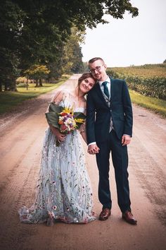 a bride and groom standing on a dirt road