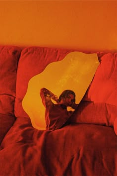 a woman laying on top of a red couch next to a yellow wall with a large piece of paper