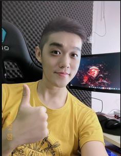 a young man giving the thumbs up sign in front of a computer screen and keyboard