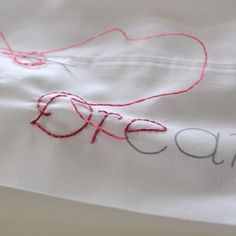 a close up of a white shirt with red thread on the bottom and words embroidered onto it