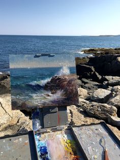 an artist's easel sitting on top of a rocky beach next to the ocean