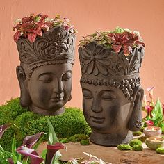 two buddha head planters sitting on top of a moss covered table next to flowers