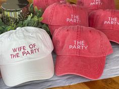 red and white hats with the words wife of the party on them next to plants