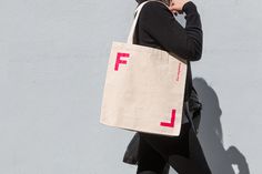 a woman walking down the street carrying a tote bag with pink letters on it