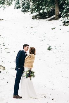 a bride and groom kissing in the snow