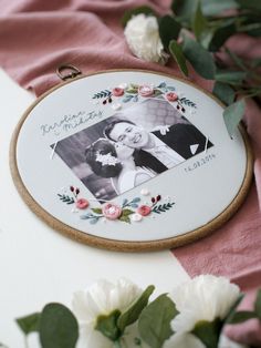 an embroidered photo frame with flowers and greenery around it on a pink table cloth