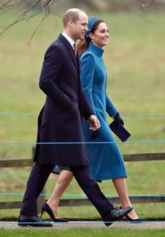 a man and woman in blue coats walk together on the grass near a fenced area