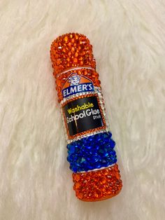 an orange, blue and red bottle with some beads on it sitting on a white surface