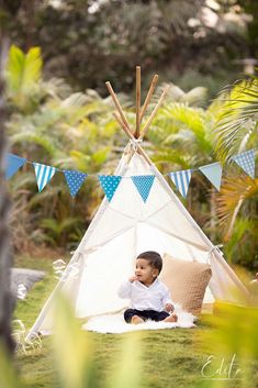 a little boy sitting in front of a teepee