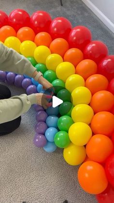 a woman is playing with balloons on the floor in front of a rainbow - colored wall