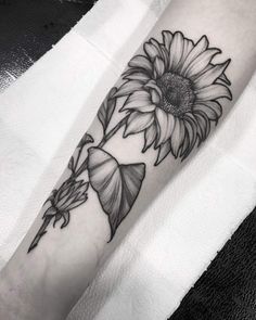 a sunflower tattoo on the left forearm and arm with leaves around it, in black and white