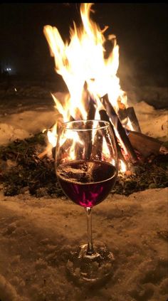 a glass of wine sitting in front of a fire pit with flames coming from it