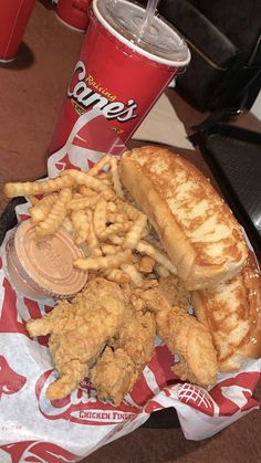 fried chicken, french fries and soda on a paper wrapper next to a red cup