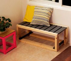 a wooden bench sitting in front of a window next to a small table with two pillows on it