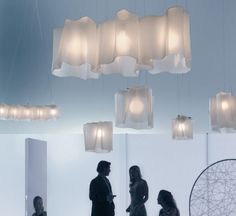 three people are standing in a room with lights hanging from the ceiling and chairs on the floor