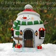 a snowman is standing in front of a small house with presents on the roof