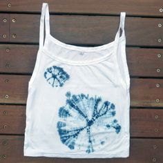 a white tank top with blue tie - dyed flowers on the front and bottom, sitting on a wooden surface