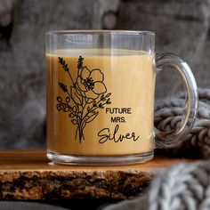 a glass mug filled with liquid sitting on top of a wooden table next to a blanket