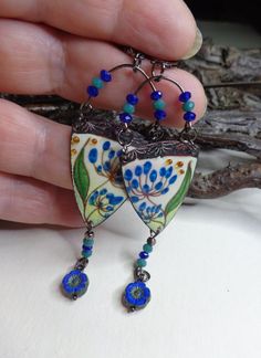 a hand holding a pair of earrings with blue beads and glass bead details on it