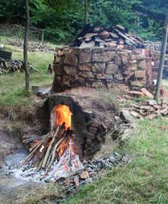 an outdoor fire pit in the middle of a field with logs and grass around it