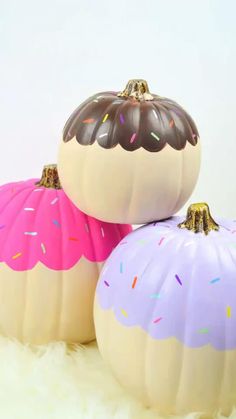 three decorative pumpkins with frosting and sprinkles on them sitting on white fur