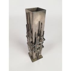 a tall metal vase with multiple knives sticking out of it's sides on a white surface