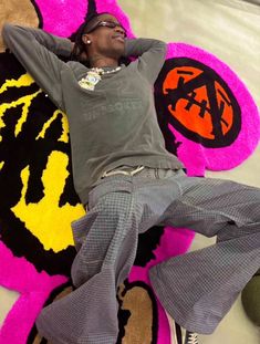 a man laying on top of a rug covered in pink and yellow designs with his hands behind his head