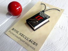 a book necklace with a red apple next to it