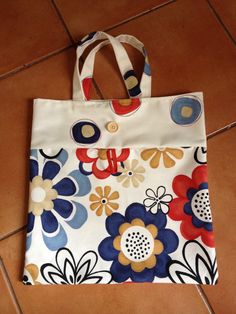 a white bag with blue, red and yellow flowers on it sitting on a tile floor