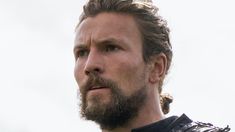 a close up of a man with a beard and leather jacket looking off to the side