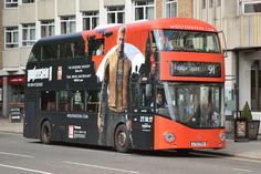 an orange and black double decker bus driving down the street in front of tall buildings