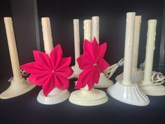 some white candles with pink flowers on them and one has a red flower in the middle