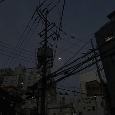 telephone poles and wires in an urban area at night, with the moon behind them