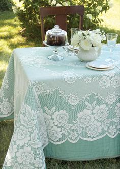 a table covered in white lace with flowers on it and a tea pot sitting on top of the table