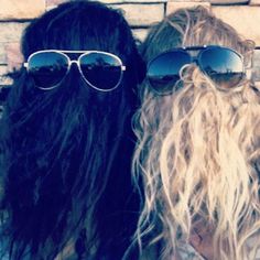 two people with long hair and sunglasses are standing next to each other in front of a brick wall