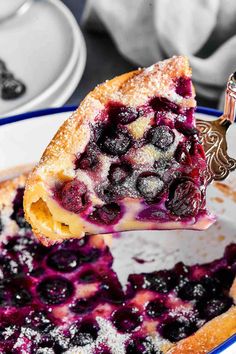 a piece of blueberry pie being lifted from a plate with powdered sugar on top