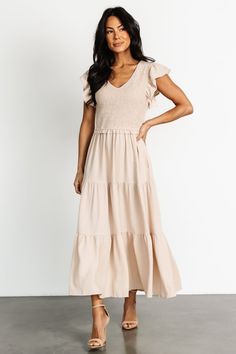 Our Afton Smocked Tiered Dress in Sand is a new staple piece for your closet. With flowy material and stretchy smocking, the Afton doesn't sacrifice comfort for style. Snag it now! Feminine Smocked Dress With Flutter Sleeve, Beige Ruched V-neck Maxi Dress, Feminine Flowy V-neck Smocked Dress, Feminine V-neck Flowy Smocked Dress, Chic V-neck Smocked Dress With Ruffle Hem, Beige V-neck Midi Dress With Ruffles, Casual V-neck Smocked Dress With Ruffles, V-neck Smocked Dress With Gathered Waist For Vacation, Chic Smocked V-neck Dress With Ruffles