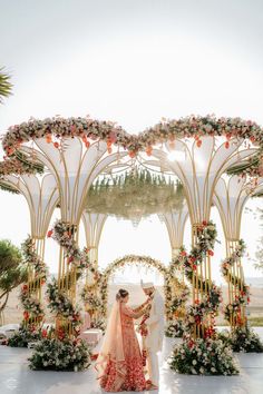 a bride and groom standing in front of an outdoor wedding ceremony arch with flowers on it