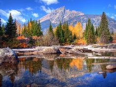 a mountain range is reflected in the still water of a lake surrounded by rocks and trees