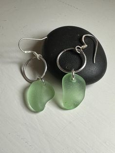 two green sea glass earrings sitting on top of a rock next to a pair of silver earwires