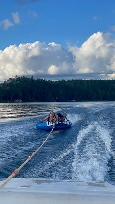 two people on a blue boat in the water with trees in the back ground and clouds in the sky