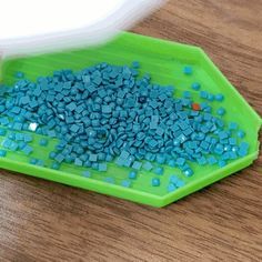 a green bowl filled with blue rocks on top of a wooden table next to a white container