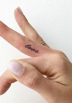 a person's hand with a small tattoo on the middle finger that says love