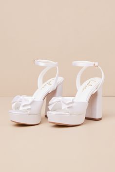 Your walk down the aisle just got even more fabulous, thanks to the Lulus Pearlla Bow White Satin Platform High Heel Sandals! These sleek satin heels feature a trendy square toe upper (atop a 1"" toe platform), and a wide toe strap adorned with a darling bow detail. Matching straps sprout from the sides to wrap and secure around the ankle with a gold buckle, all atop a sky-high block heel that is sure to take your look to the next level! 4. 5" wrapped block heel. Cushioned insole. Felted rubber White High Heels For Quinceanera, White Wedges Heels, High Heels For Graduation, White Shoes With Bow, Confirmation Heels, White Heels Simple, Plain White Heels, Formal Heels Classy, Satin Sandals With Wrapped Heel